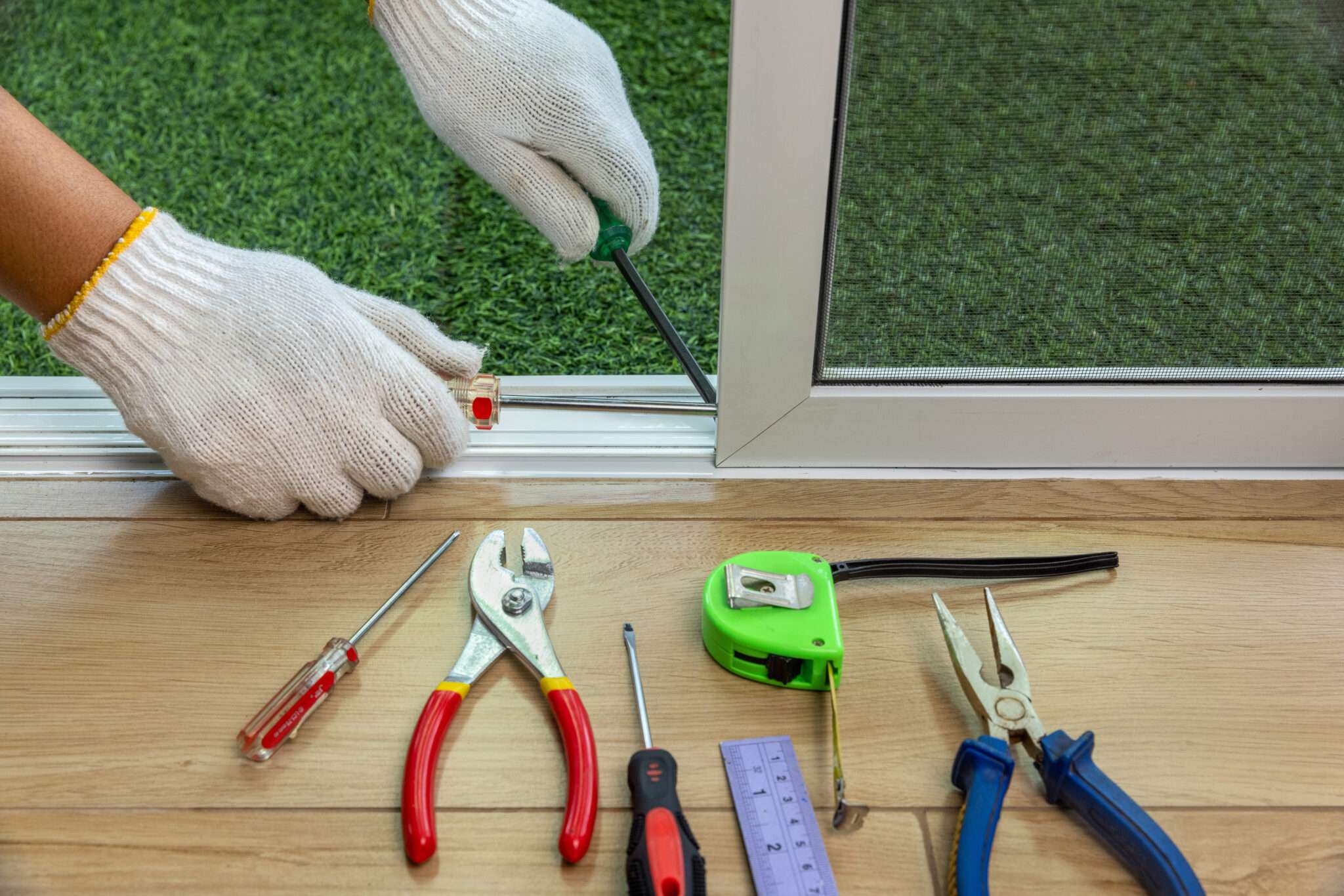 Gloved hands fixing screen door with tools