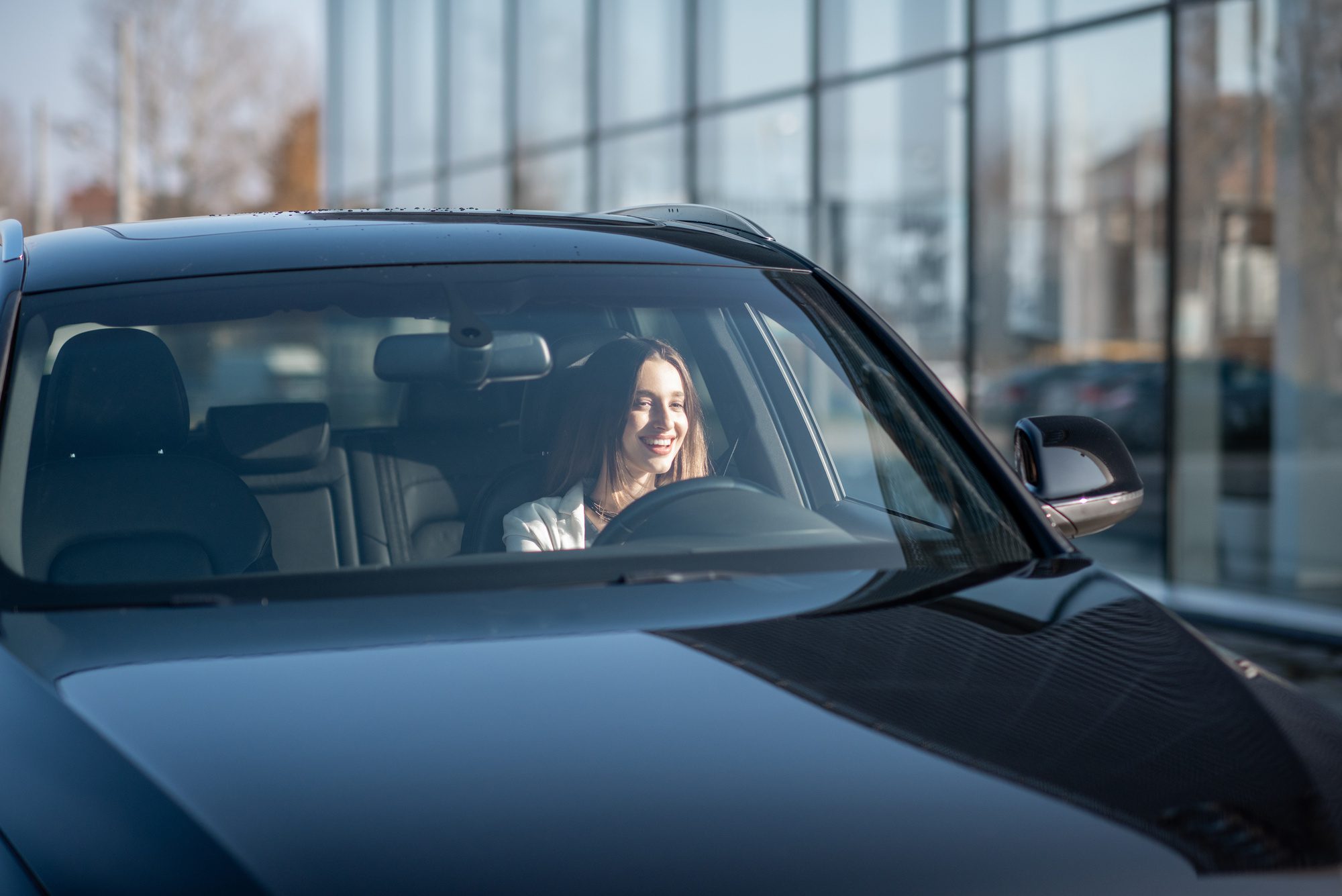 Young woman smiling and driving a black car with a clear windshield