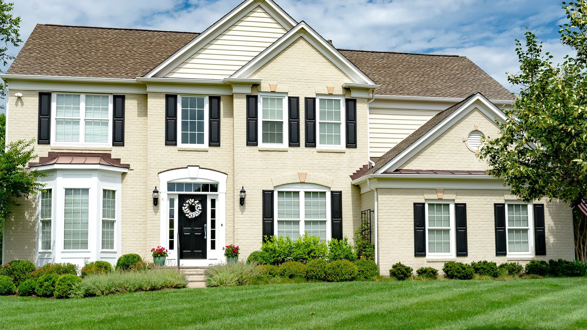 Exterior view of home with off-white brick and vinyl siding, black exterior door, and beautiful new windows by GoGlass