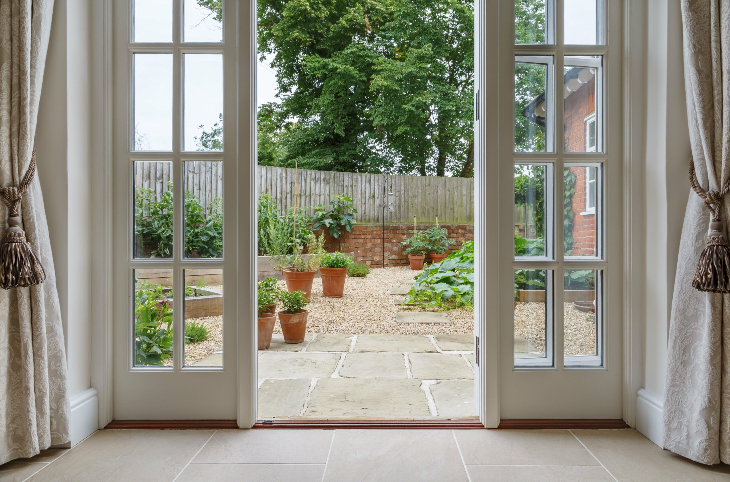 A patio door is opened up and there are plants in the backyard